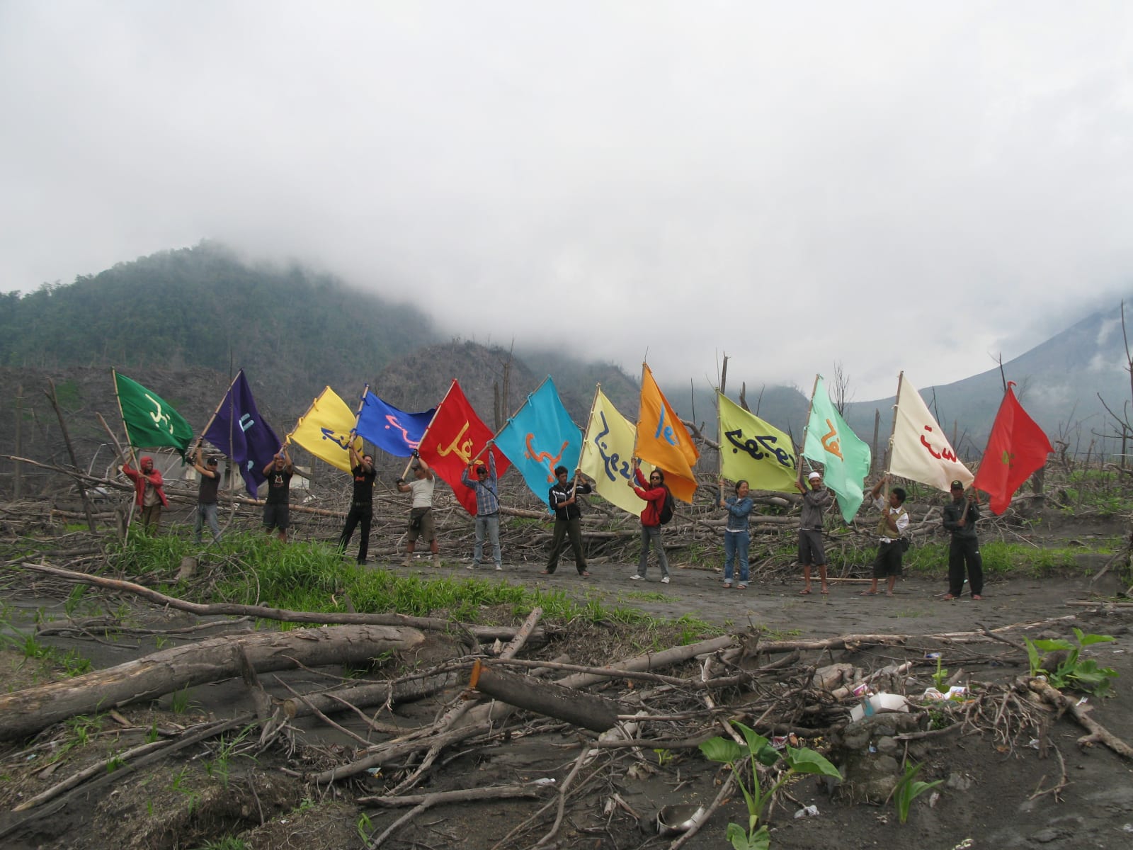 A large group holds colorful flags in an open field